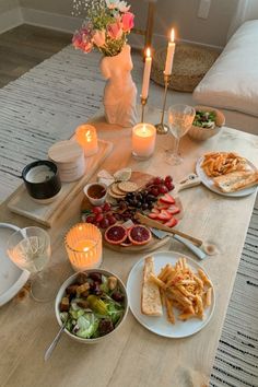 a wooden table topped with plates and bowls filled with food next to candlelight candles