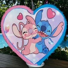 a heart shaped balloon with stitch and stitch characters painted on the front, sitting on a wooden bench