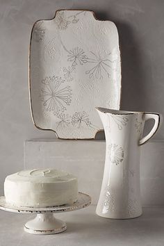 a white cake sitting on top of a plate next to a vase and tray with flowers