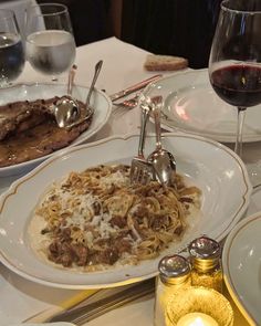 a table topped with plates of food next to glasses of wine and utensils