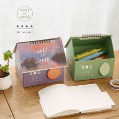 an open notebook sitting on top of a wooden table next to a box filled with pencils