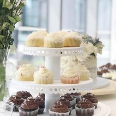 cupcakes and cakes are on a white cake stand with flowers in the background