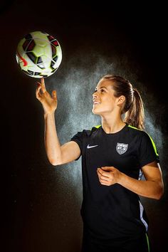 a woman holding a soccer ball in her right hand and spraying water on her face