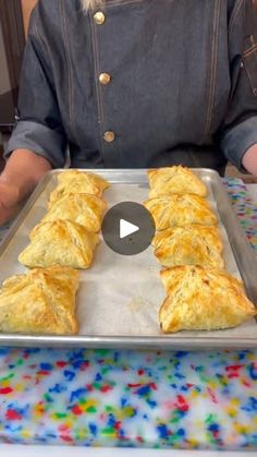 a woman in an apron is holding a tray with pastries on it and the video appears to be being viewed