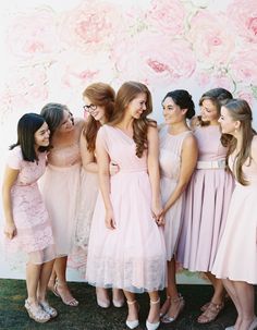 a group of women standing next to each other in front of a wall with flowers on it