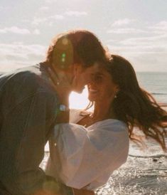 a man and woman kissing on the beach in front of the ocean with sun flares