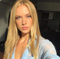 a woman with long blonde hair and blue eyes posing in front of a car window