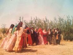 a group of people standing next to each other on a dirt field with trees in the background