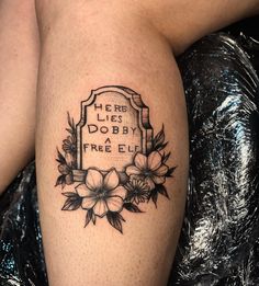 a tattoo on the leg of a woman with flowers and a tombstone in the background