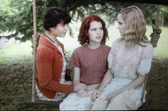 three young women sitting on a swing in the woods, one is talking to another woman