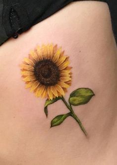 a yellow sunflower tattoo on the side of a woman's stomach with green leaves