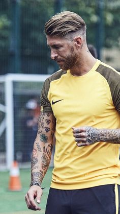 a man with tattoos on his arm and chest wearing a yellow shirt, black shorts