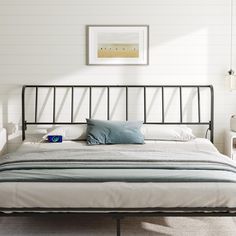 a bedroom with a metal bed frame and blue pillows on the top of it, in front of a white wall