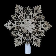 an intricate wooden snowflake is shown on a white vase with blue base and black background