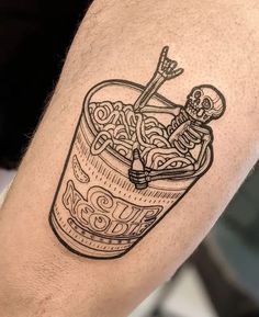 a man's arm with a tattoo on it and a cup filled with noodles