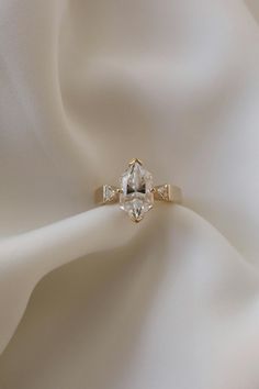 an engagement ring on top of a white satin fabric with the center stone in yellow gold