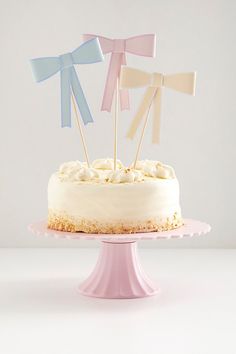 a cake with white frosting and three small bows on top, sitting on a pink plate