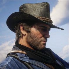 a man wearing a cowboy hat and blue shirt looks off into the distance with clouds in the background