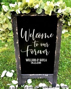 a welcome sign with greenery on it in front of the grass and flowers behind it