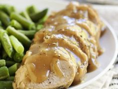 a white plate topped with meat covered in gravy next to green beans