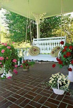 a white bench sitting on top of a brick floor next to potted plants and flowers