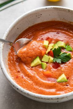 a white bowl filled with tomato soup and avocado garnish