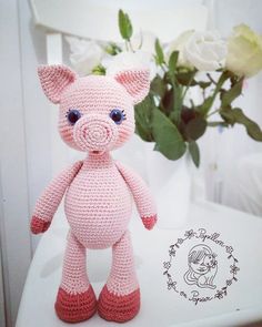 a pink crocheted pig sitting on top of a table next to a vase with flowers