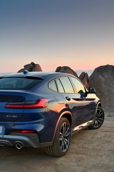 the rear end of a blue bmw suv parked in front of some rocks and boulders