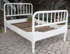 a white bed frame sitting on top of a brick floor