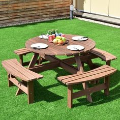 a wooden picnic table with two benches and plates on it in the middle of grass