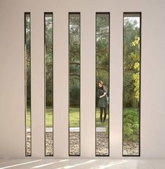 a woman standing in front of three tall windows with trees and grass behind her on the other side