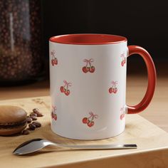 a red and white coffee mug sitting on top of a wooden table next to a spoon