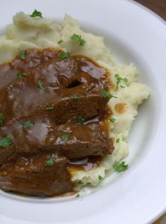 a white plate topped with mashed potatoes and beef on top of gravy