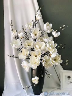 a black vase filled with white flowers on top of a table