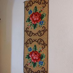 a cross stitched wall hanging on the side of a white wall next to a door