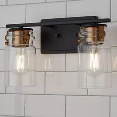 two light fixtures mounted on the wall above a white tiled bathroom counter top with black and gold accents