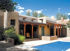 an adobe style house with a pool in the foreground and trees on either side