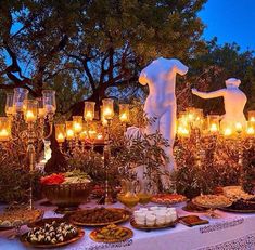 a table topped with lots of food and lit candles next to a statue in the background