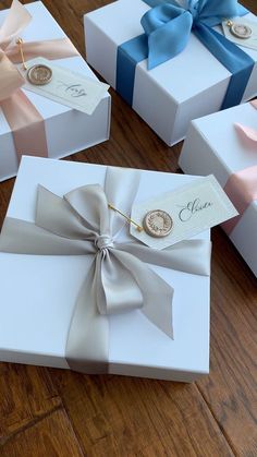 four white boxes with pink, blue and gold ribbons tied around the top one box has a name tag on it