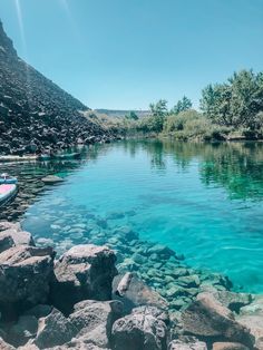 the water is crystal blue and there are rocks on the shore next to it,