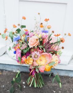 a bouquet of flowers sitting on the ground next to a white door with orange and blue flowers