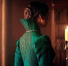 the back of a woman's green dress standing in front of a lit candle