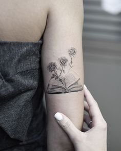 a woman's arm with a book and flowers tattoo on her left arm,