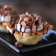 two desserts on a black plate with chocolate drizzled on top and toppings