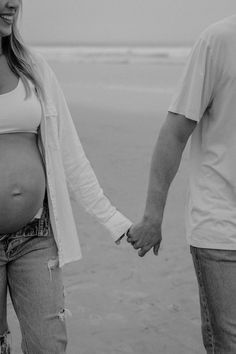 a pregnant woman holding her husband's hand on the beach