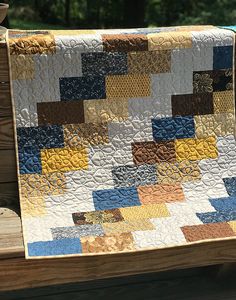 a quilt on a wooden bench with trees in the background