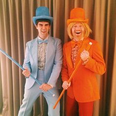 two men in orange suits and blue hats posing for the camera with one holding a cane