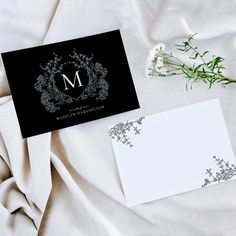 a black and white monogrammed wedding stationery on a bed with floral accents