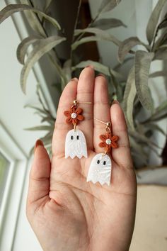 a person holding two white ghost earrings in their hand with flowers on the ear wires