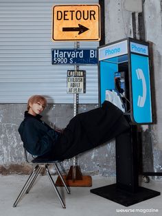 a man sitting in a chair next to a parking meter and phone booth with a detour sign on it